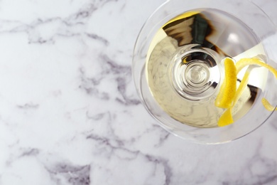 Glass of lemon drop martini cocktail with zest on white marble table, top view. Space for text