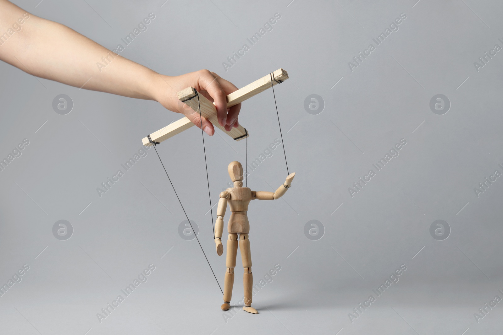 Photo of Woman pulling strings of puppet on light grey background, closeup