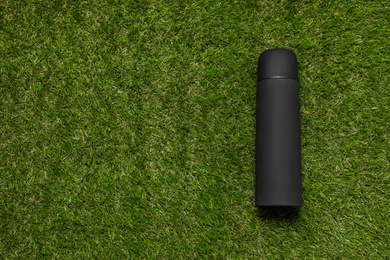 Photo of Modern black thermos on green grass, top view. Space for text