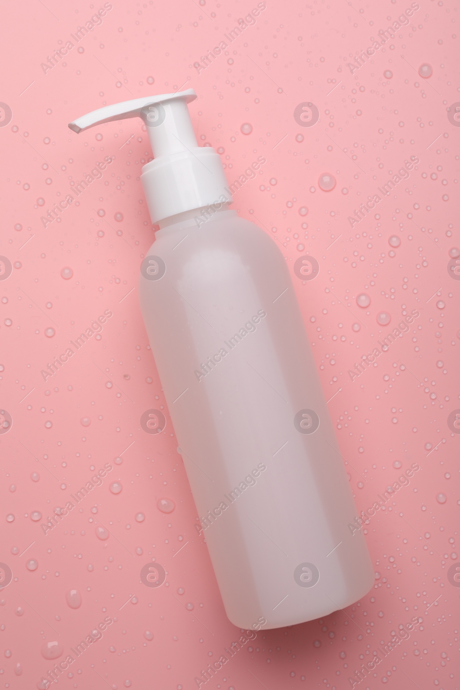 Photo of Wet bottle of face cleansing product on pink background, top view