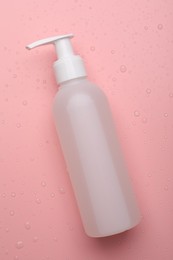 Wet bottle of face cleansing product on pink background, top view