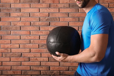 Athletic man with medicine ball near red brick wall, closeup. Space for text