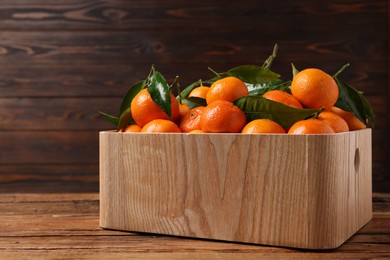 Photo of Fresh tangerines with green leaves in crate on wooden table