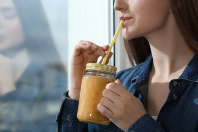 Beautiful young woman drinking delicious smoothie near window, closeup. Space for text