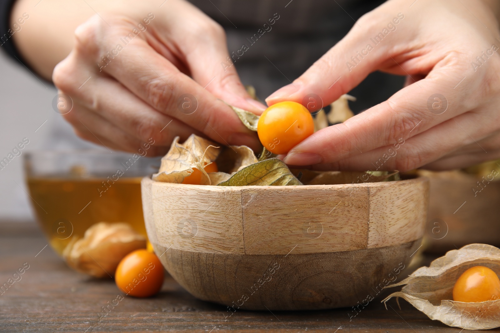 Photo of Woman peeling physalis fruit from calyxes at wooden table, closeup