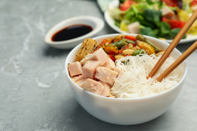 Photo of Tasty cooked rice noodles with chicken and vegetables on grey marble table