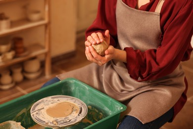 Woman crafting with clay over potter's wheel indoors, closeup