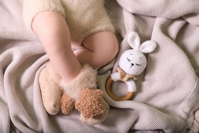 Photo of Cute newborn baby in knitted booties with toy bunny lying on light grey plaid, top view
