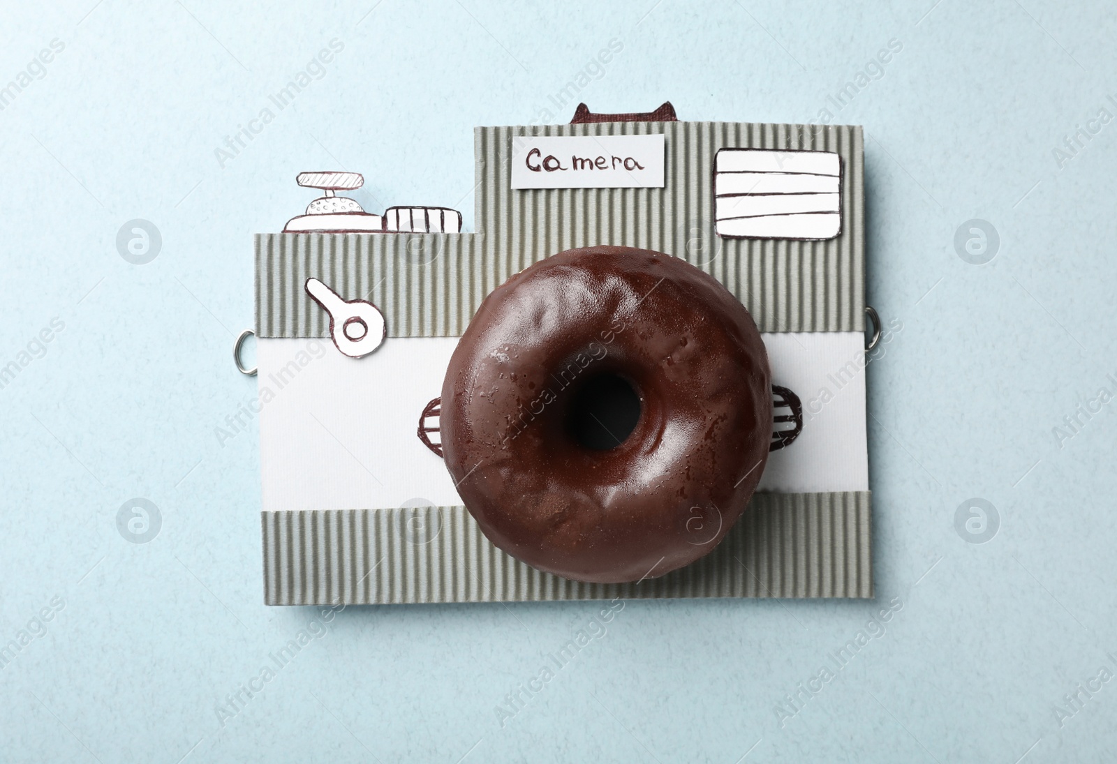 Photo of Camera made from donut and piece of cardboard on light blue background, top view