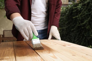 Photo of Man applying wood stain onto wooden surface outdoors, closeup