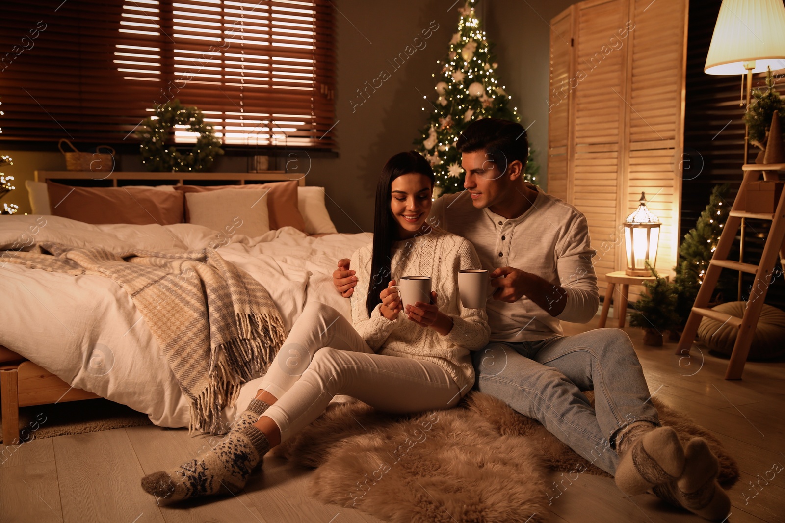 Photo of Happy couple with cups in festively decorated bedroom. Christmas celebration