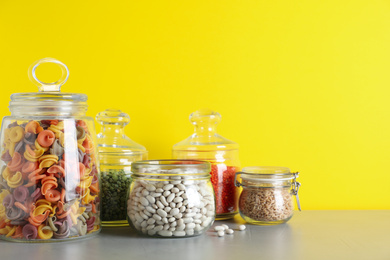 Photo of Glass jars with different types of groats and pasta on light grey table