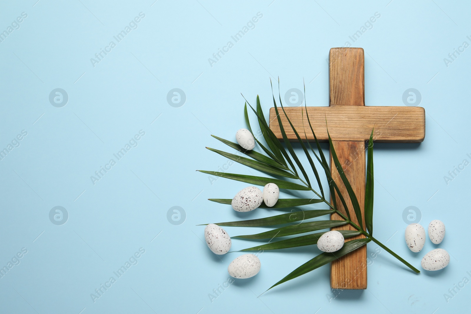 Photo of Wooden cross, painted Easter eggs and palm leaf on light blue background, flat lay. Space for text