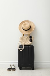 Suitcase packed for trip, shoes and summer accessories near white wall indoors