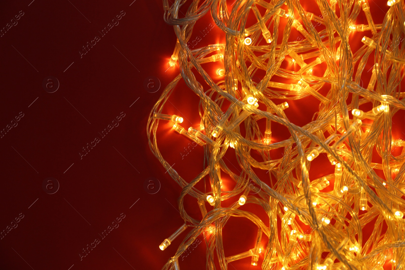 Photo of Glowing Christmas lights on red background, top view. Space for text