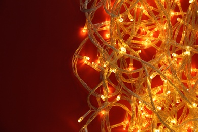 Photo of Glowing Christmas lights on red background, top view. Space for text