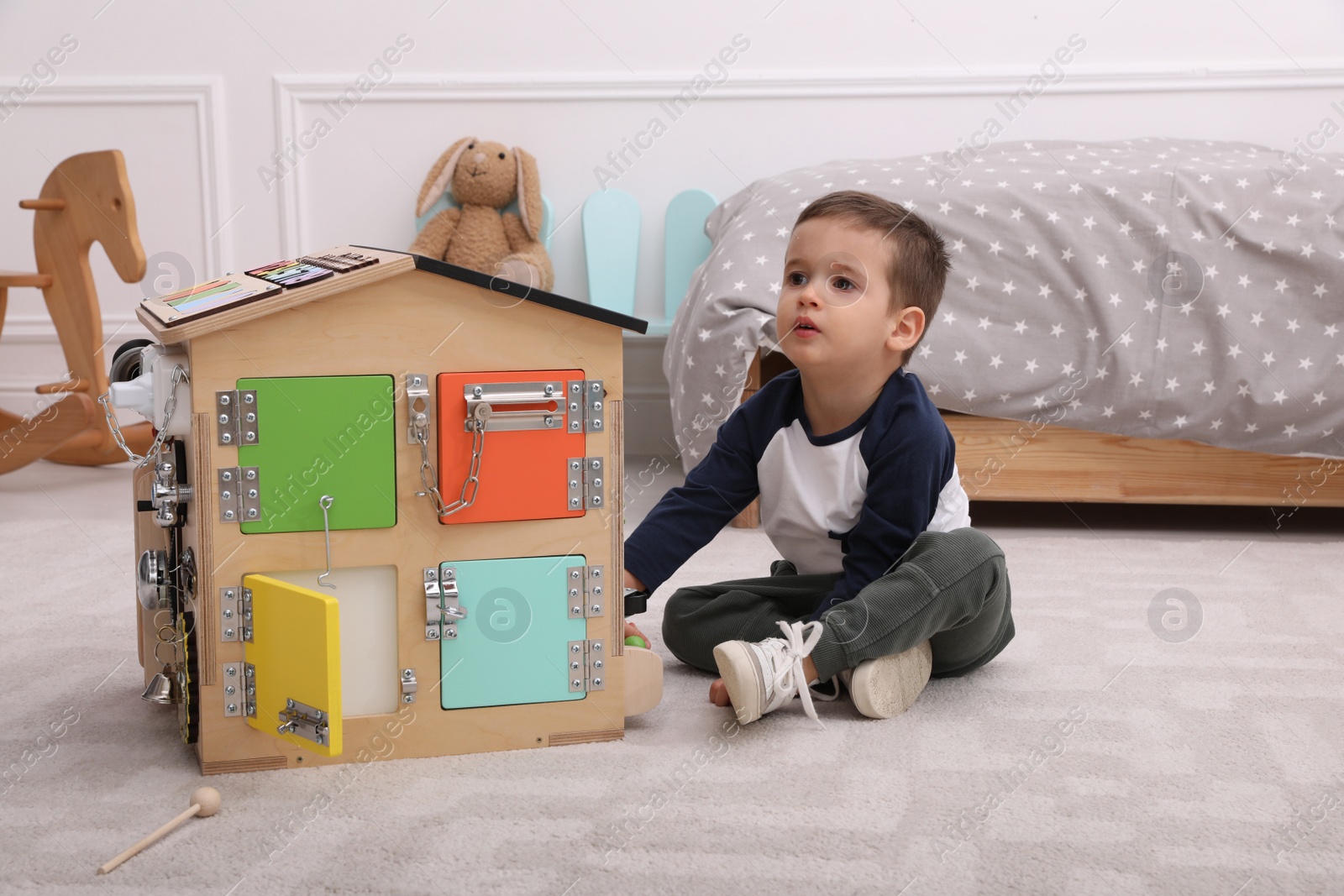 Photo of Little boy playing with busy board house on floor at home