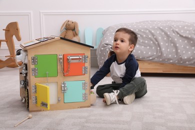 Little boy playing with busy board house on floor at home