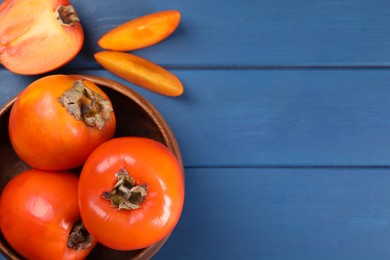 Photo of Delicious ripe persimmons on blue wooden table, top view. Space for text