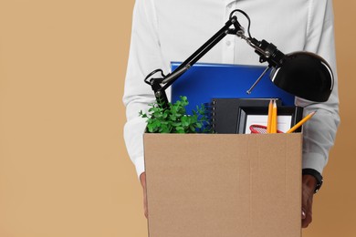 Photo of Unemployed young man with box of personal office belongings on beige background, closeup. Space for text
