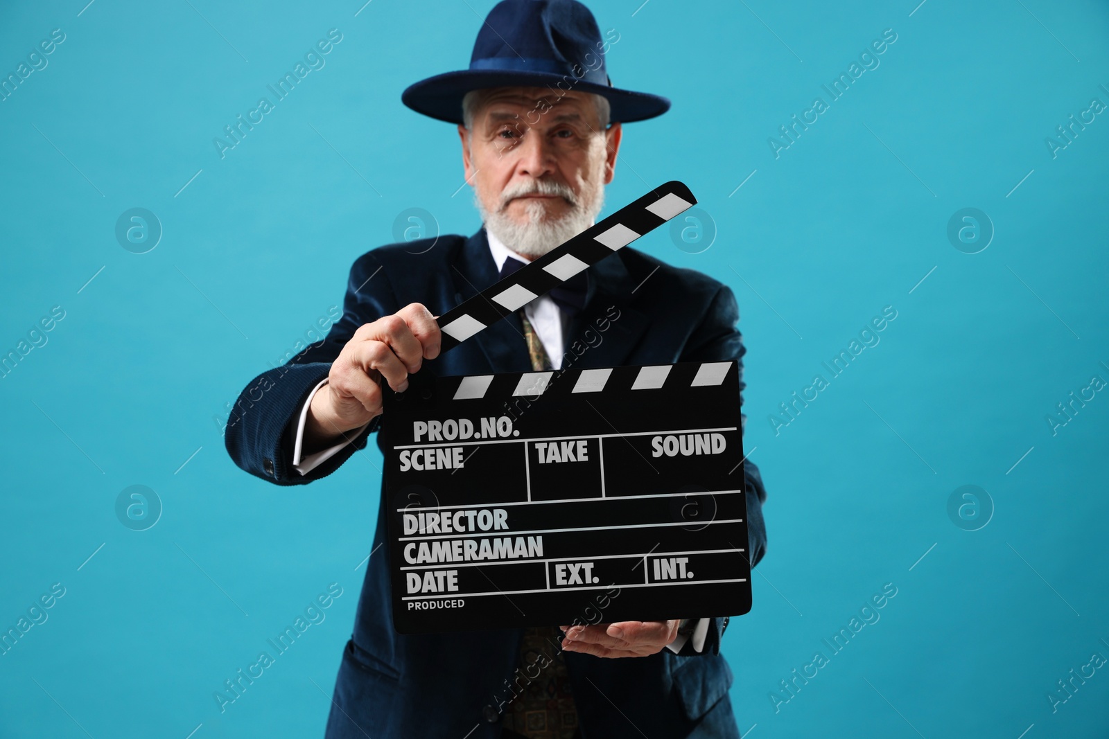 Photo of Senior actor with clapperboard on light blue background, selective focus. Film industry