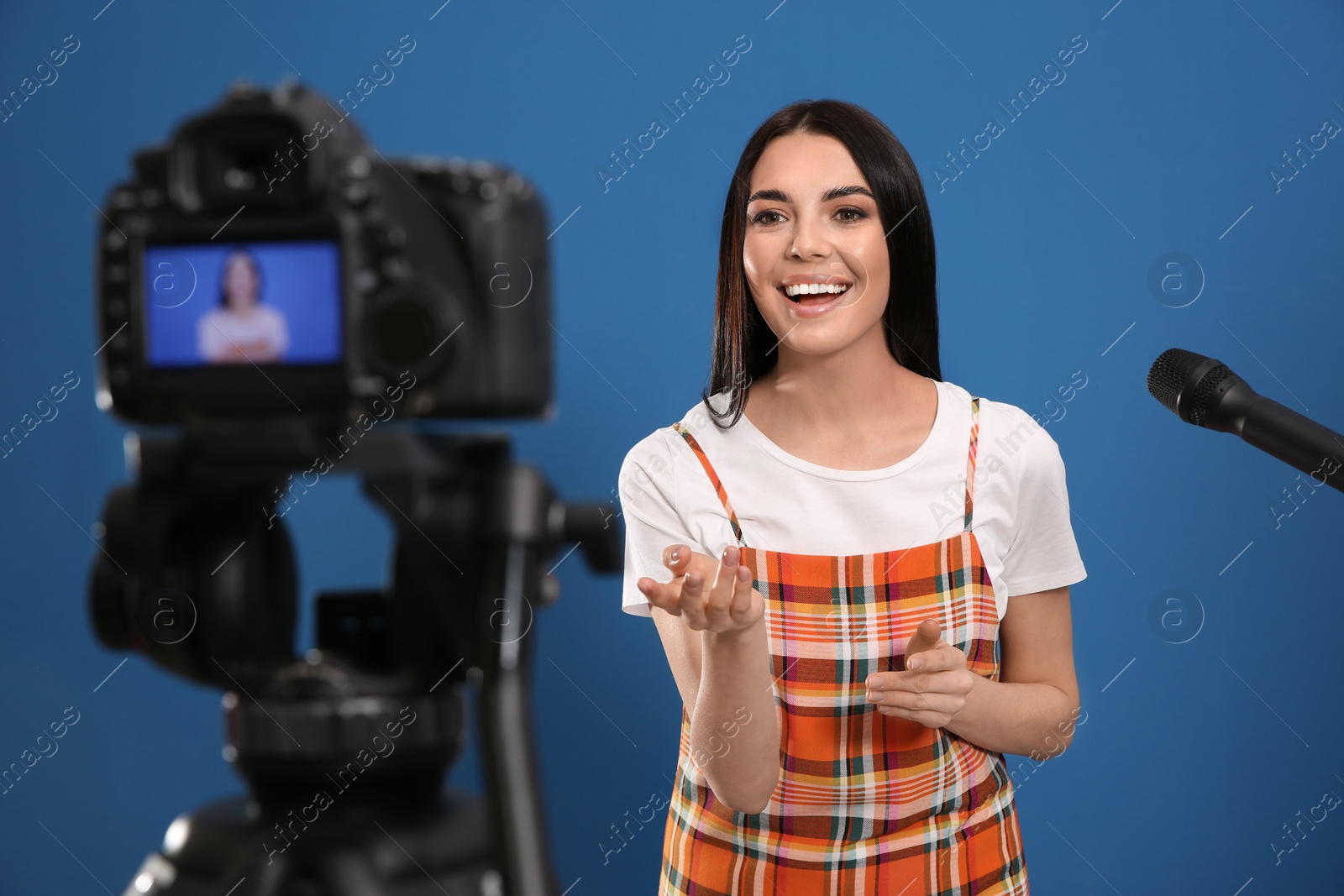 Photo of Young blogger with microphone recording video on camera against blue background