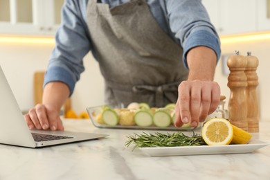 Photo of Man making dinner while watching online cooking course via laptop kitchen, closeup