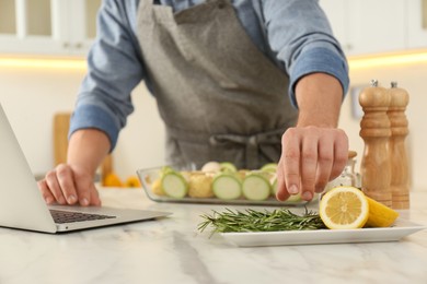 Man making dinner while watching online cooking course via laptop kitchen, closeup