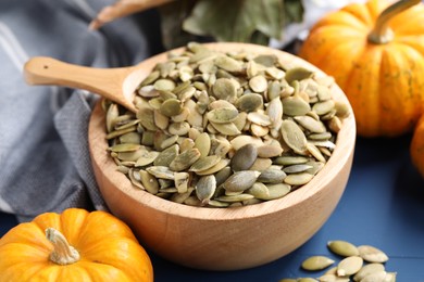 Photo of Bowl with seeds, spoon and fresh pumpkins on blue wooden table, closeup