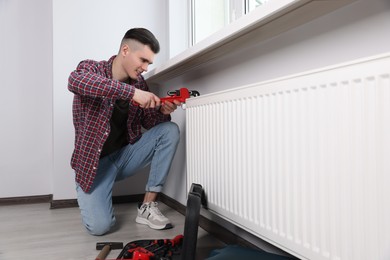 Man fixing radiator with pipe wrench in room