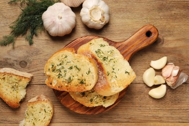 Tasty baguette with garlic and dill on wooden table, flat lay