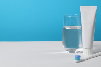 Photo of Plastic toothbrush with paste and glass of water on white table against light blue background, space for text