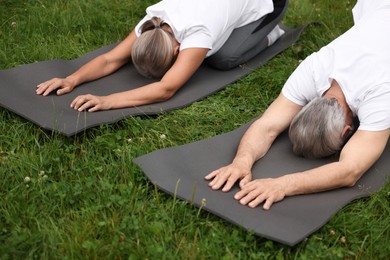 Photo of Senior couple practicing yoga on green grass outdoors