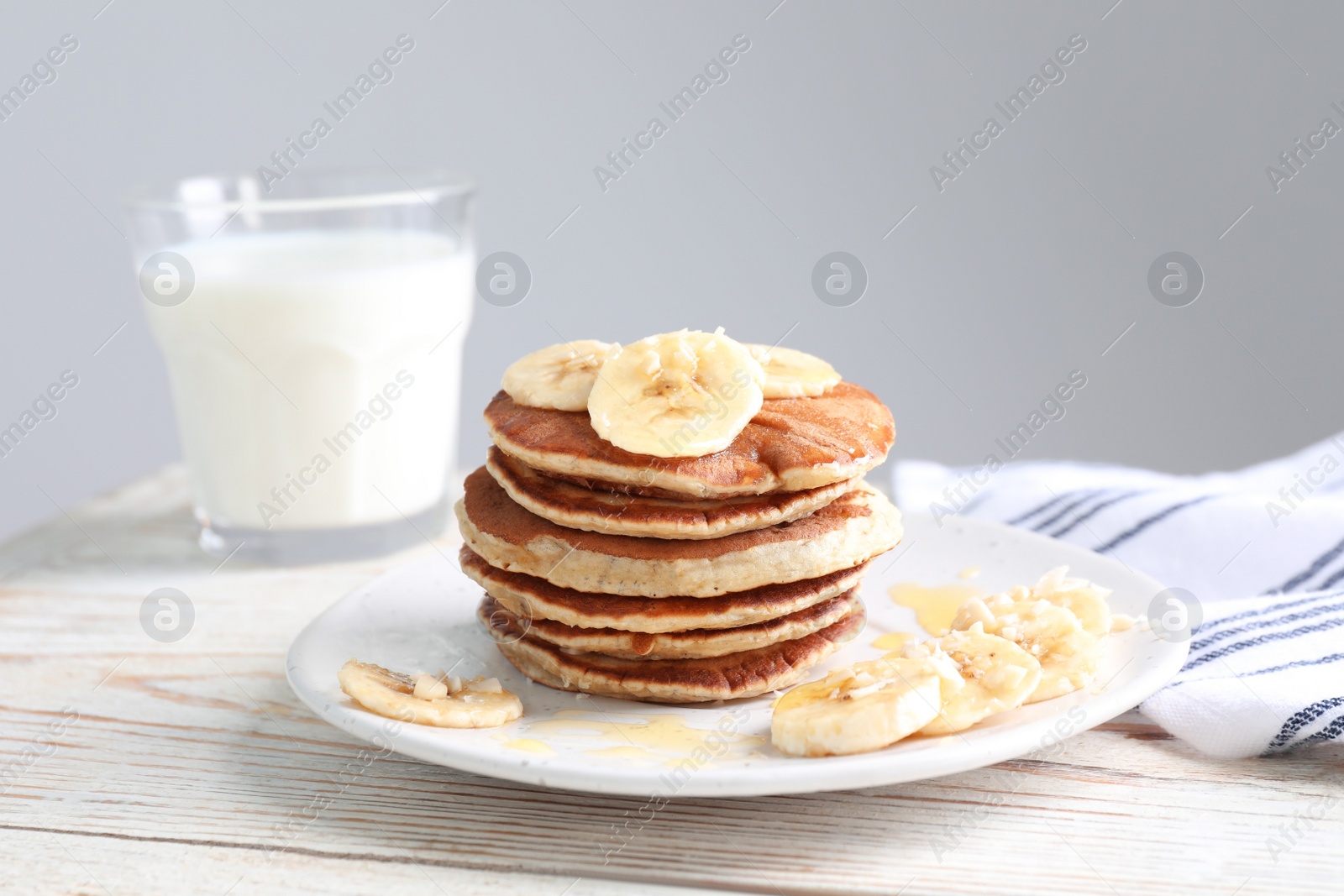 Photo of Plate of banana pancakes with honey on white wooden table