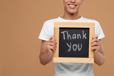 Photo of Man holding small chalkboard with phrase Thank You on brown background, closeup. Space for text