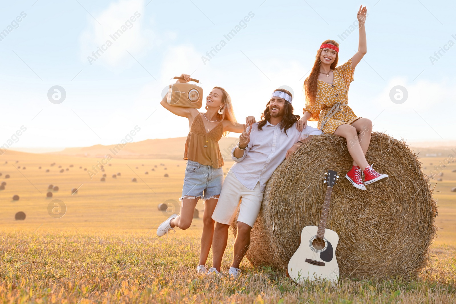 Photo of Happy hippie friends with radio receiver and guitar in field, space for text