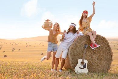 Happy hippie friends with radio receiver and guitar in field, space for text