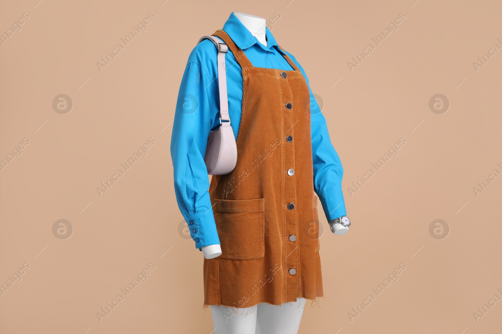 Photo of Female mannequin with accessories dressed in light blue shirt and orange jumper dress on beige background