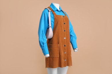 Female mannequin with accessories dressed in light blue shirt and orange jumper dress on beige background