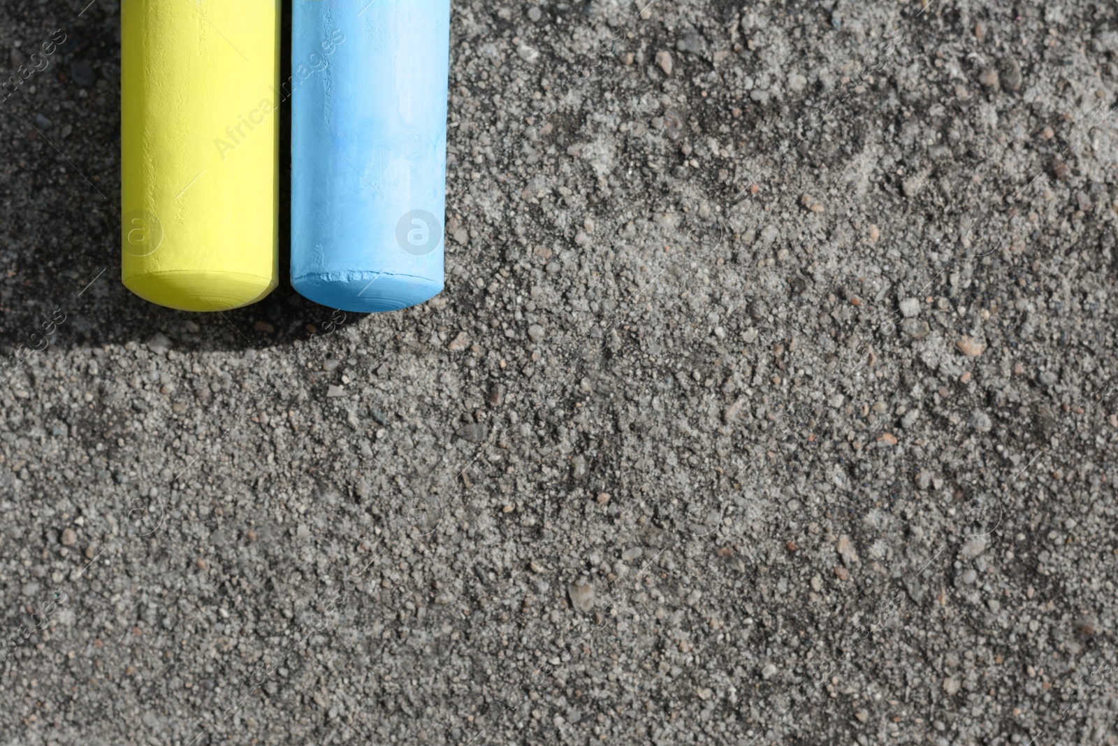 Photo of Yellow and light blue chalk sticks on asphalt, flat lay. Space for text