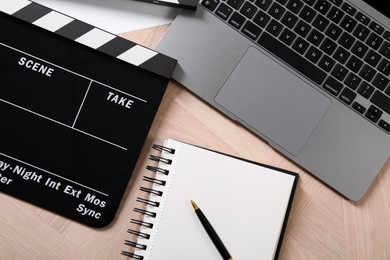 Photo of Movie clapper, notebook, laptop and pen on wooden table, flat lay