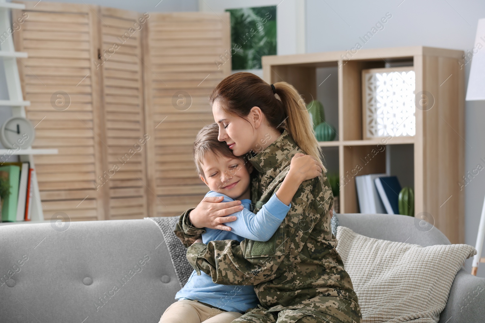 Photo of Woman in military uniform with her little son on sofa at home