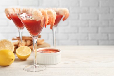 Tasty shrimp cocktail with sauce in glasses and lemon on light wooden table, space for text