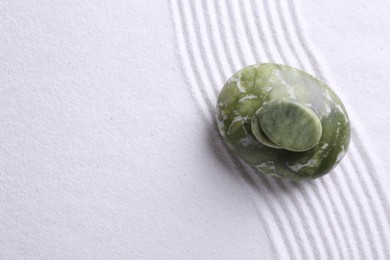 Photo of Zen garden stones on white sand with pattern, top view. Space for text