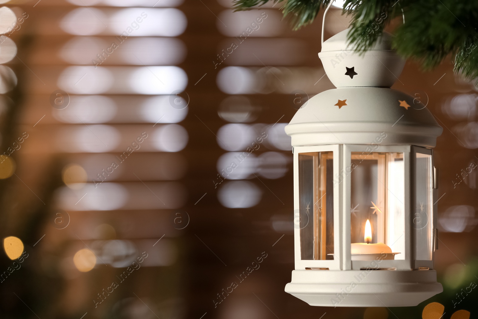 Photo of Beautiful Christmas lantern with burning candle hanging on fir tree branch in room. Space for text