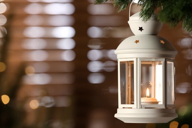 Photo of Beautiful Christmas lantern with burning candle hanging on fir tree branch in room. Space for text