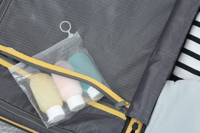 Photo of Plastic bag of cosmetic travel kit and clothes in suitcase, top view. Bath accessories