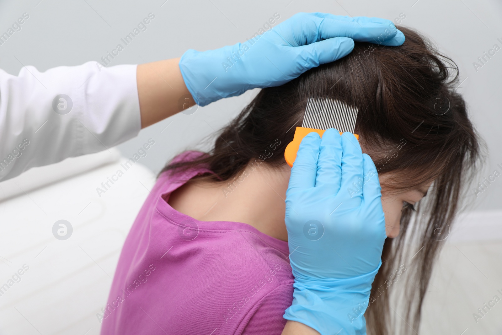 Photo of Doctor using nit comb on little girl's hair indoors. Anti lice treatment