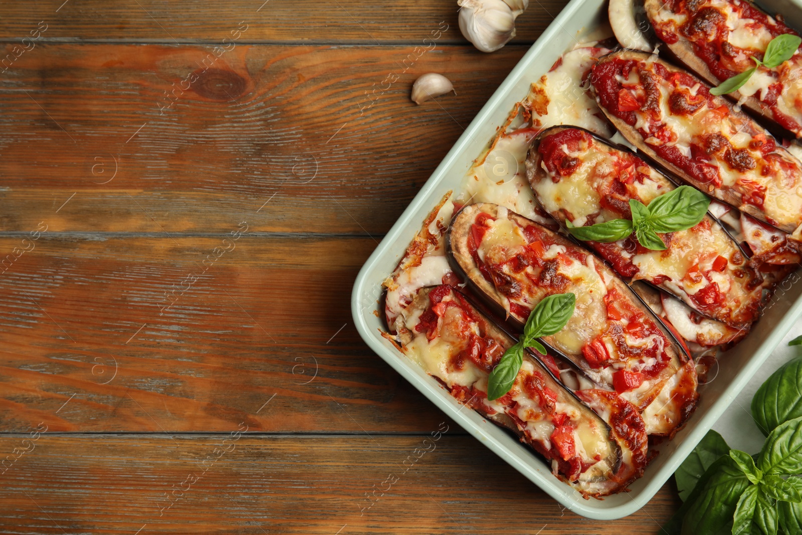 Photo of Baked eggplant with tomatoes, cheese and basil in dishware on wooden table, flat lay. Space for text
