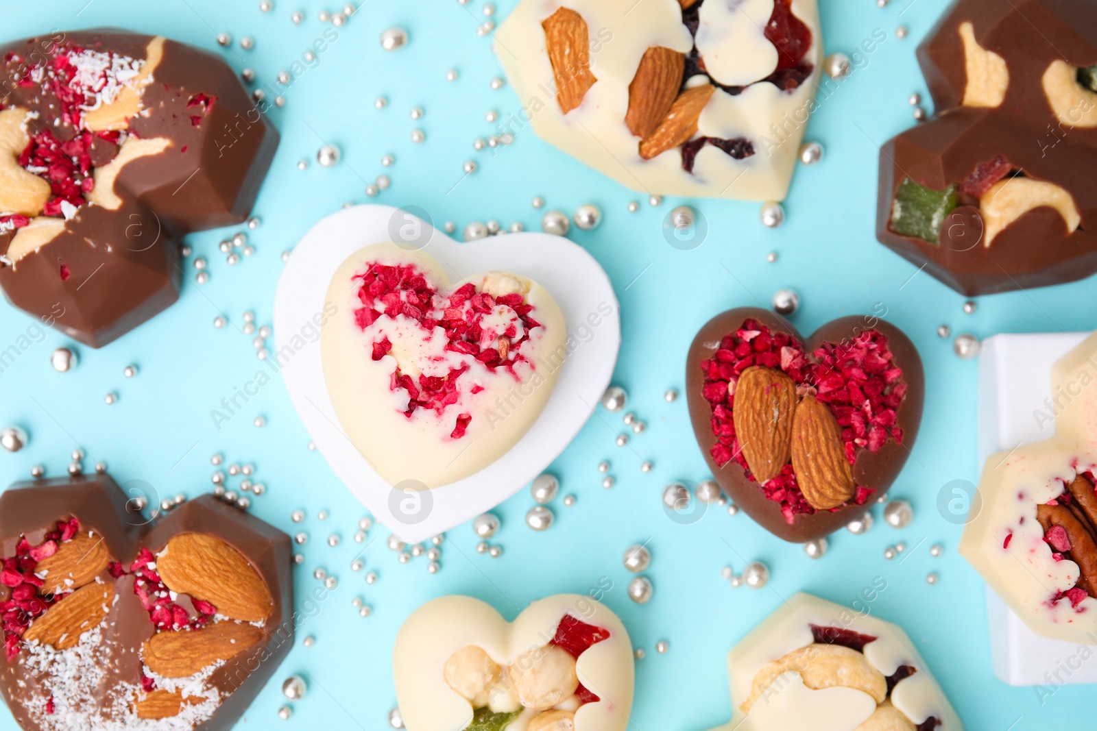 Photo of Tasty chocolate heart shaped candies with nuts on light blue background, flat lay